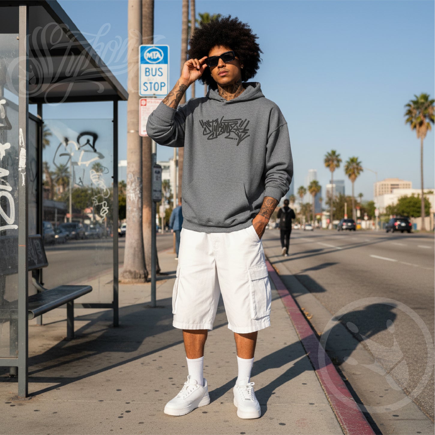 Person wearing a grey hoodie with Stykonz embroidery design, white shorts, and white sneakers on a city street.