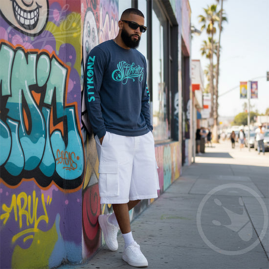 Man wearing a navy sweatshirt with Stykonz brand logo, white shorts, and white sneakers leaning against a colorful graffiti wall.