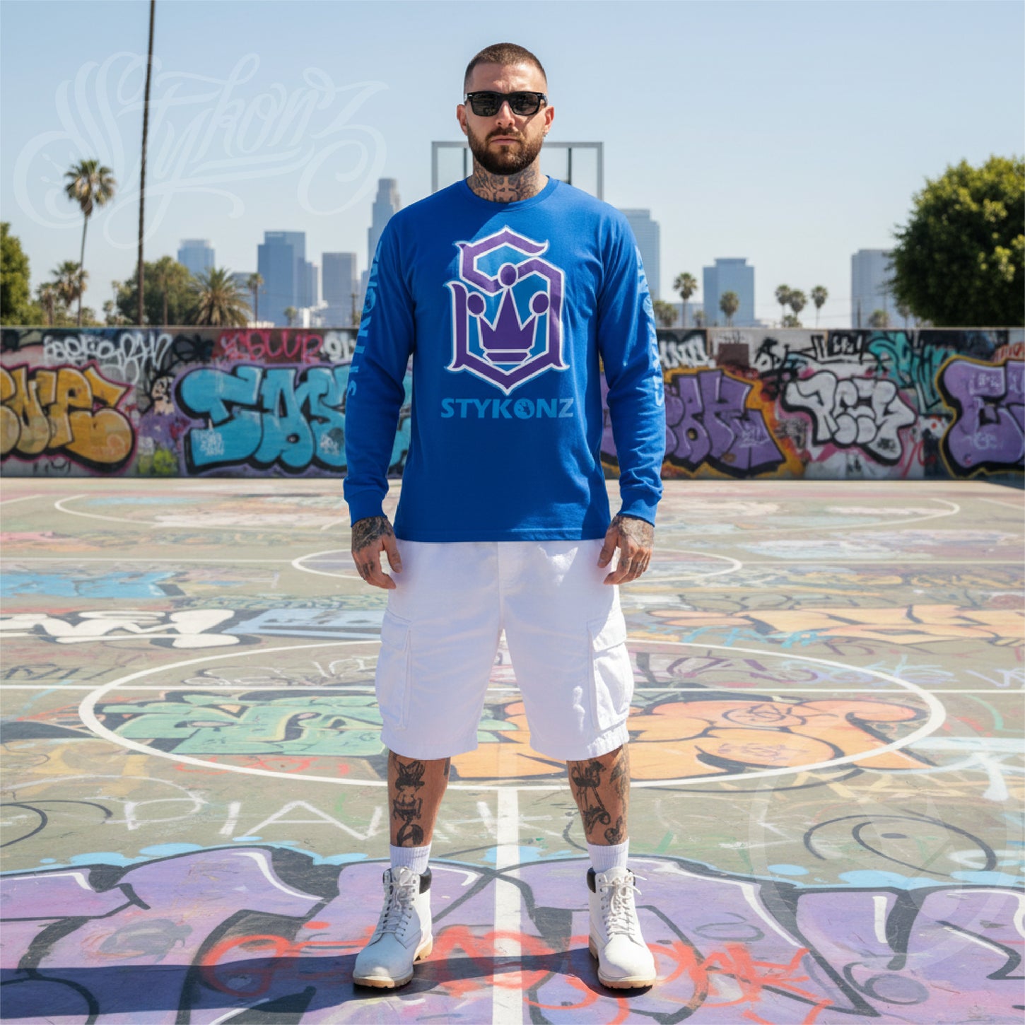 A man wearing a blue long-sleeve shirt with Stykonz design on a graffiti-covered basketball court.