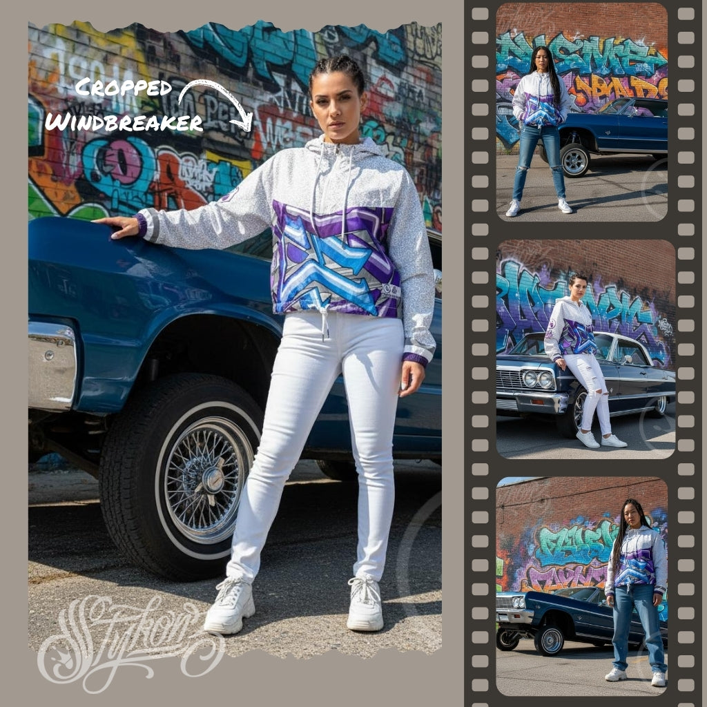 A woman wearing a graffiti-designed windbreaker and white pants is standing next to a blue Chevy Impala with graffiti in the background.